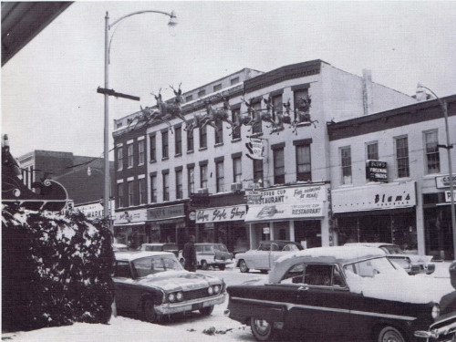 Black and white photo of Main Street storefronts with parked cars